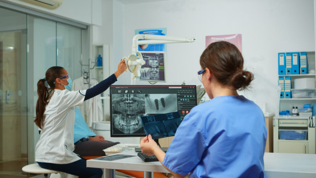 Dental Digital Imaging Workstation › TECHBLEED Dental professional reviewing dental X-rays on a monitor while holding a tablet