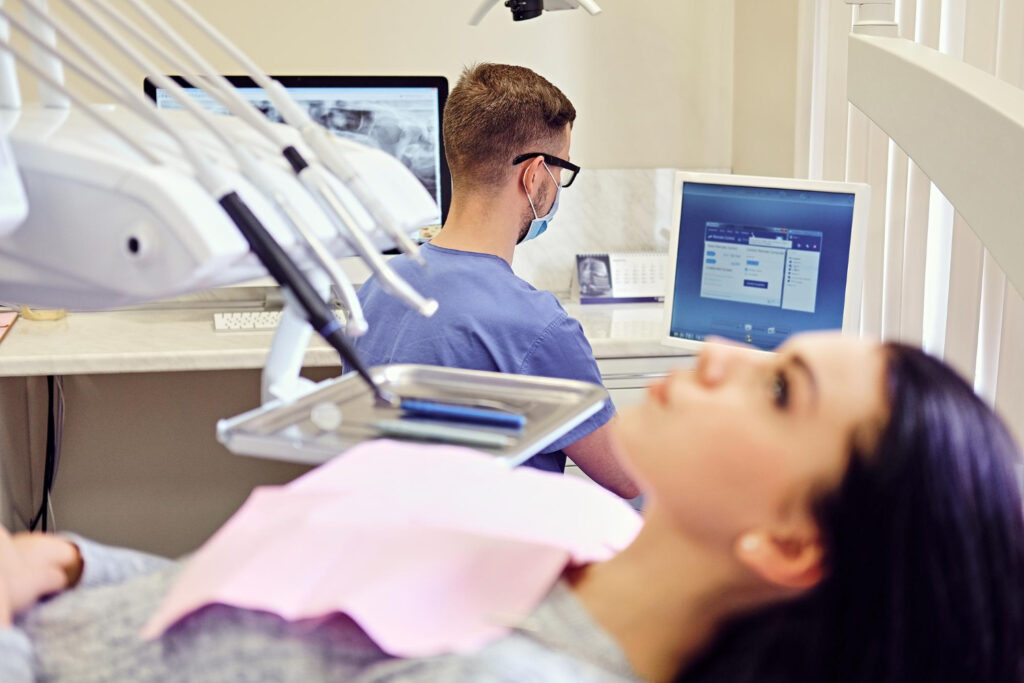 Dental Practice Computer Systems › TECHBLEED Dentist using a computer while a patient sits in a dental chair